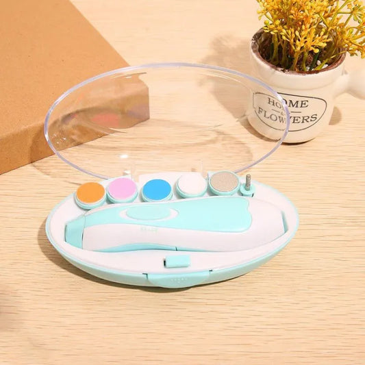 A mint green and white electric nail care set with five colorful attachments (orange, pink, blue, white, silver) in an oval case with a transparent lid, placed on a wooden surface beside a small potted plant labeled “Home Flowers.”